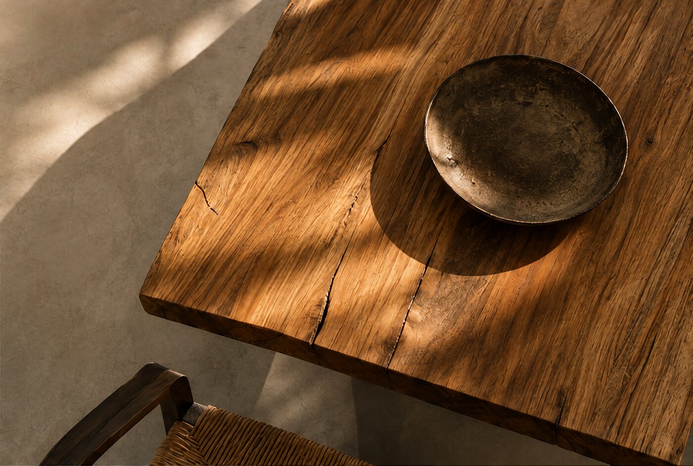 Looking down onto the corner of a Suar table, the grain and one long fissure crossing it, a dark bowl in the raking light