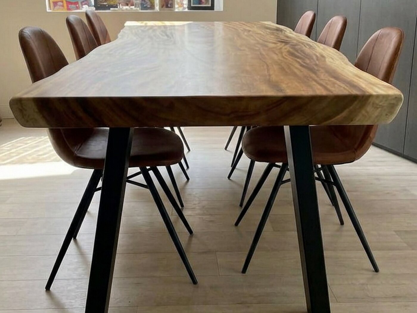 The table seen end-on, chairs drawn in down both sides, a deep window reveal to the left and daylight across the pale floor