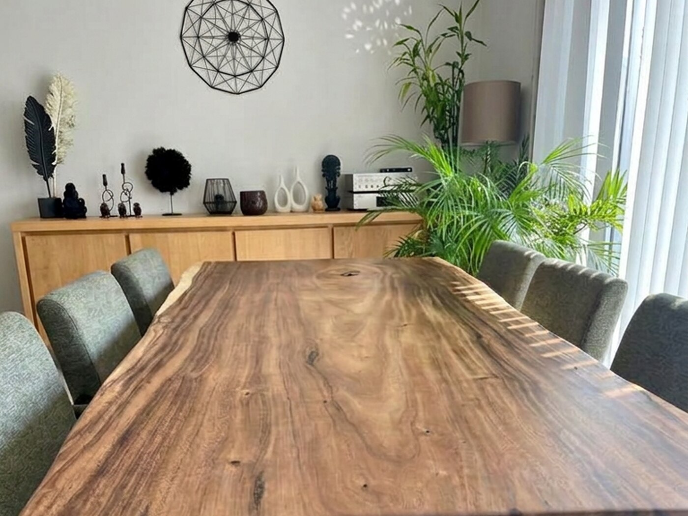 The table across a pale tiled floor, an oak sideboard and a palm behind it and full-height sheer curtains to the right